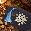 Schneeflocken-Lesezeichen aus silberfarbenem Metall mit hellblauer Quaste auf einem Fantasy-Buch
